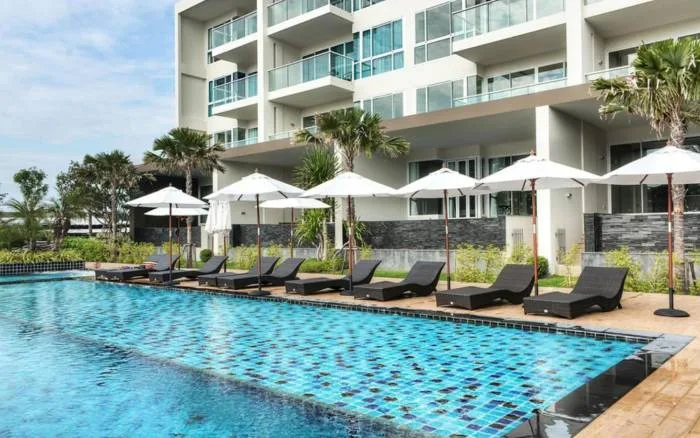 Cetus Beachfront outdoor swimming pool with blue mosaic tiles, lounge chairs, and white umbrellas.