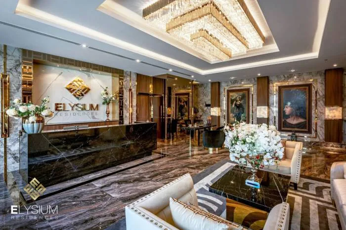 Elysium Residences grand lobby with marble reception desk, large chandelier, and luxurious seating.