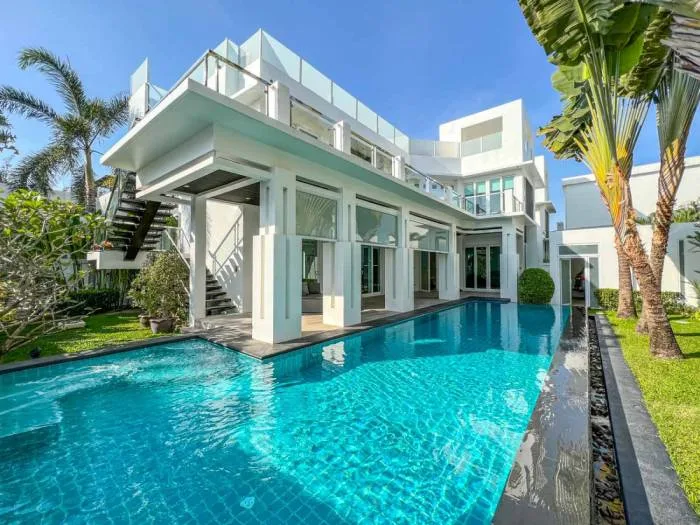 Palm Oasis Villas modern white house with a large swimming pool, green lawn, and tropical palm trees under a blue sky.