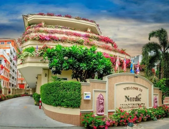 Nordic Residence entrance with colorful flowering balconies, lush greenery, and a 'Welcome to Nordic Residence' sign.