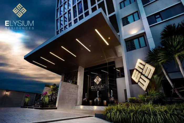Elysium Residences modern building entrance at dusk with illuminated canopy and logo.