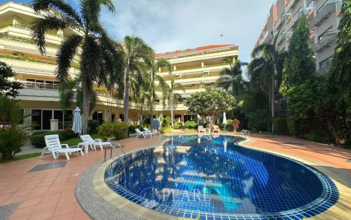 Nordic Residence aerial view of a dolphin-shaped swimming pool surrounded by tropical palm trees and lush flowering plants.