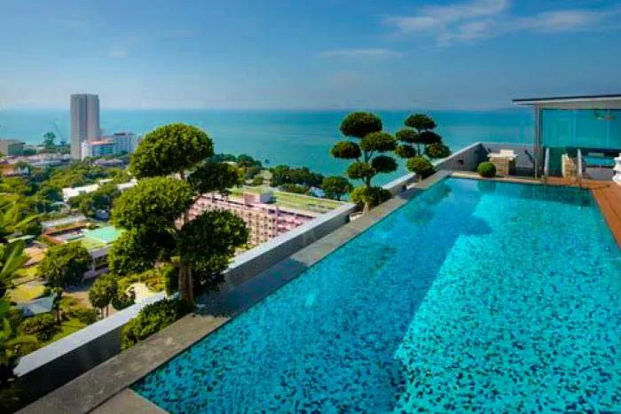 One Tower Pratumnak rooftop infinity pool overlooking the city skyline and ocean under a clear blue sky.