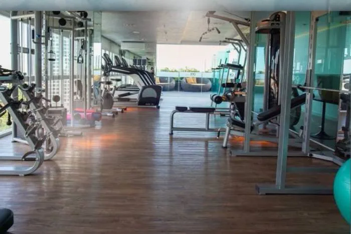 One Tower Pratumnak indoor gym with various exercise machines, wooden floor, and large windows to an outdoor lounge.