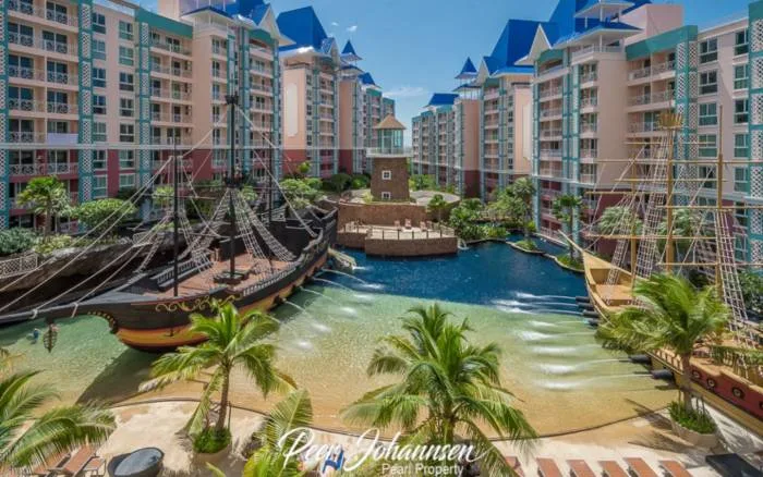 Grande Caribbean resort with pirate ships, sandy beach pool, and colorful buildings under a blue sky.