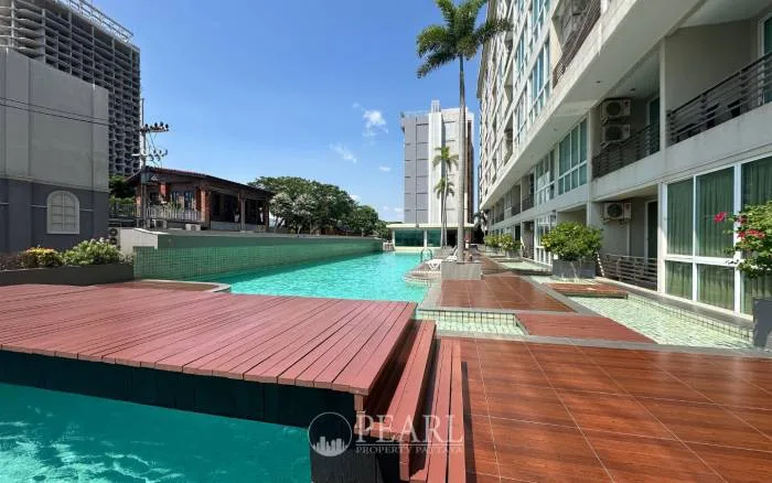 Musselana long swimming pool with sun loungers, wooden decking, and the modern condo building facade.