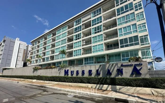 Musselana large swimming pool with a decorative bridge, palm trees, and the condo building under a blue sky.