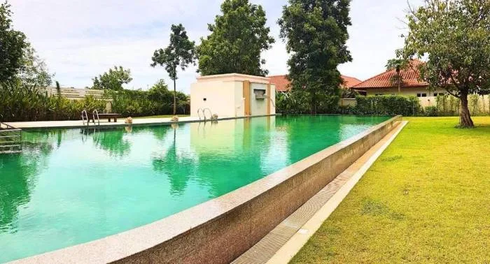 Baan Balina 2 large outdoor swimming pool with green water, surrounded by a lush green lawn and tropical trees.