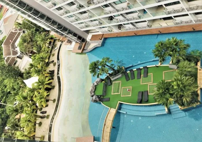 Laguna Beach Resort 1 overhead view of the lagoon pool, artificial beach, and sun loungers on a green island.