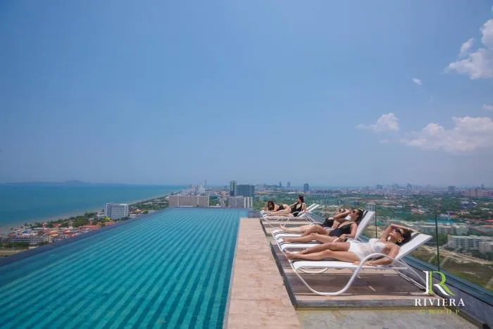 The Riviera Jomtien illuminated exterior at dusk, showcasing the brightly lit windows and 'THE RIVIERA' sign against a twilight sky.