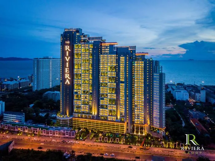 The Riviera Jomtien full exterior view of the tall condo building with 'THE RIVIERA' signage, facing a busy road and the ocean.