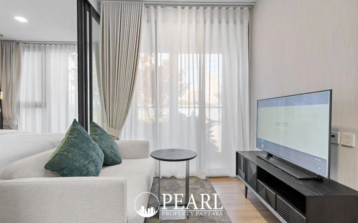 1 Bedroom Condo for Sale at Aquarous Jomtien Pattaya: Living area with a sofa, side table, TV, and large windows with curtains.