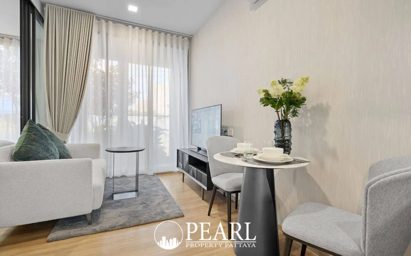 1 Bedroom Condo for Sale at Aquarous Jomtien Pattaya: Living and dining area with small table, two chairs, sofa, and TV.