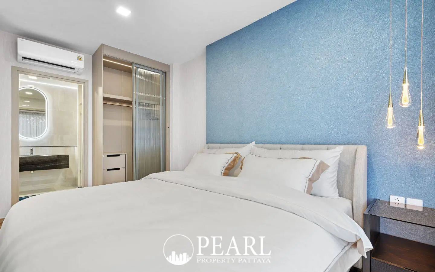 1 Bedroom Condo for Sale at Aquarous Jomtien Pattaya: Bedroom with blue accent wall, white bed, open closet, and bathroom entrance.