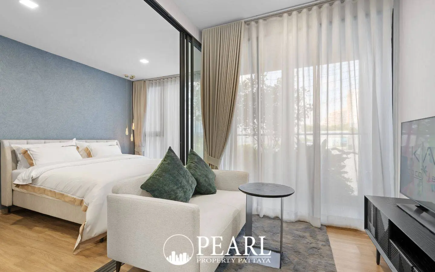 1 Bedroom Condo for Sale at Aquarous Jomtien Pattaya: Bedroom with white bedding, small sofa, and large windows with sheer curtains.