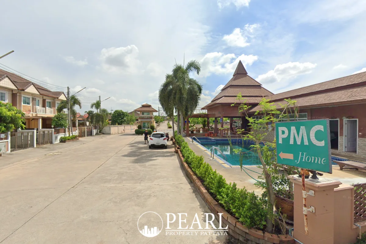 PMC Village 2 street view showing houses, a communal swimming pool, and a clubhouse with a tiered roof.