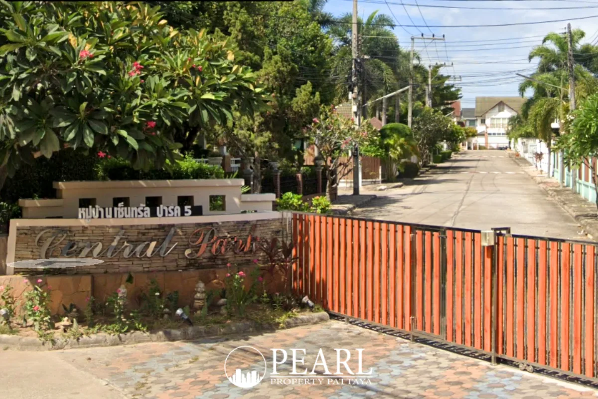 Central Park 5 Village entrance sign with orange gate and paved road leading into the village.