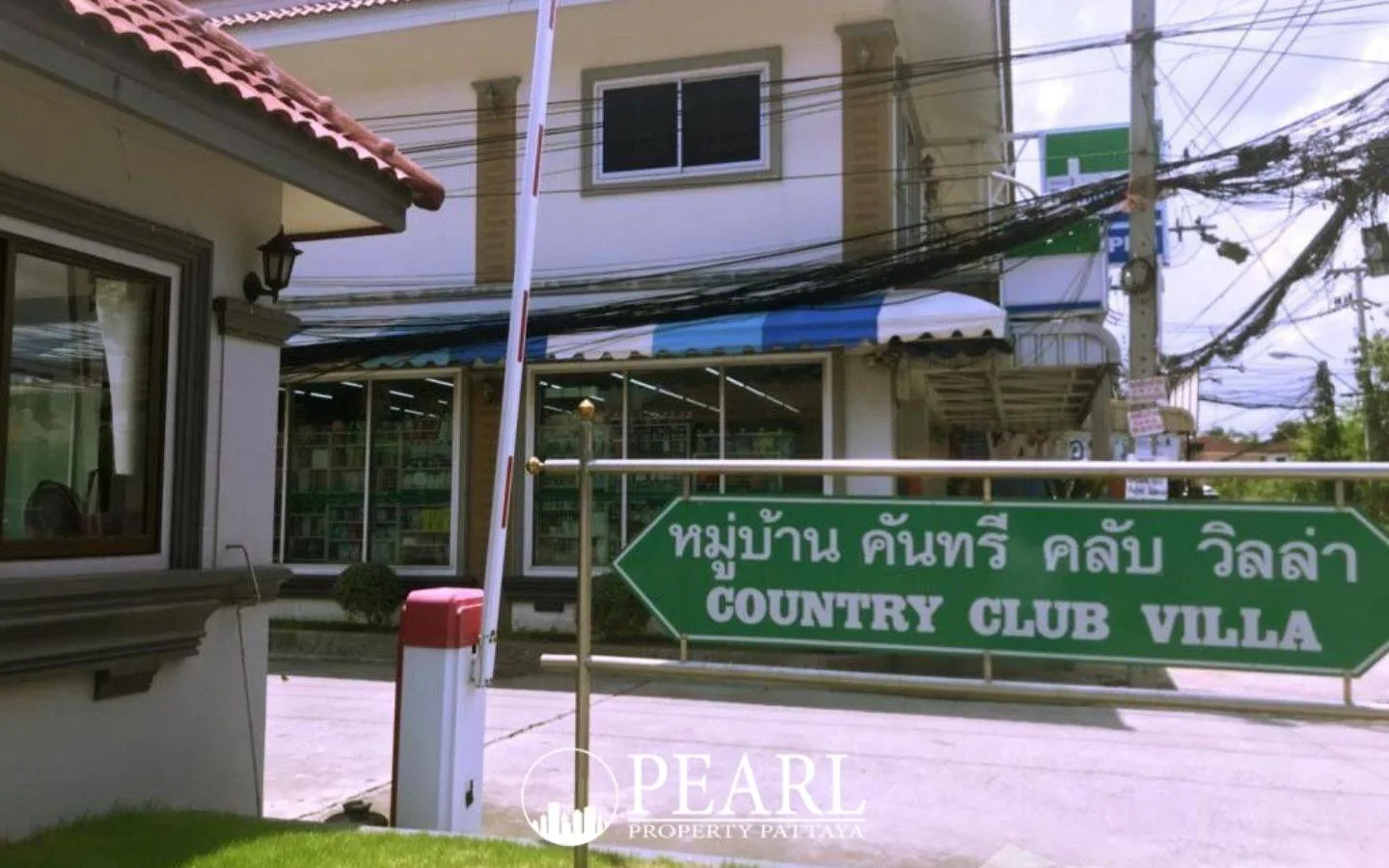 Country Club Villa entrance gate with a green sign and a convenience store in the background.