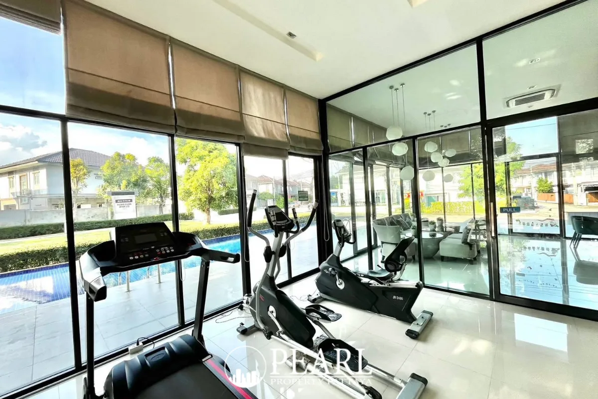 Baan Pruksa Nara Chaiyapruek modern fitness center with gym equipment and large windows overlooking a pool.