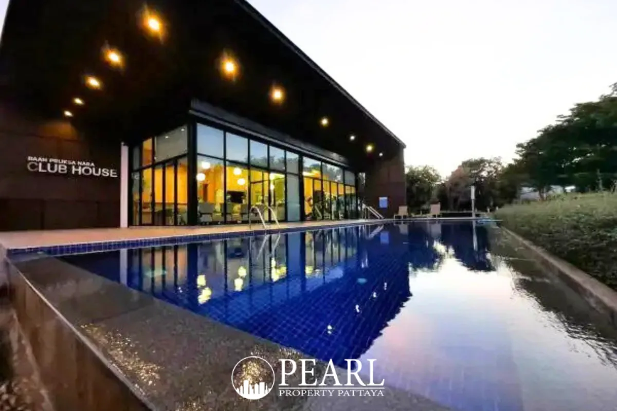 Baan Pruksa Nara Chaiyapruek outdoor swimming pool with a modern clubhouse at dusk.