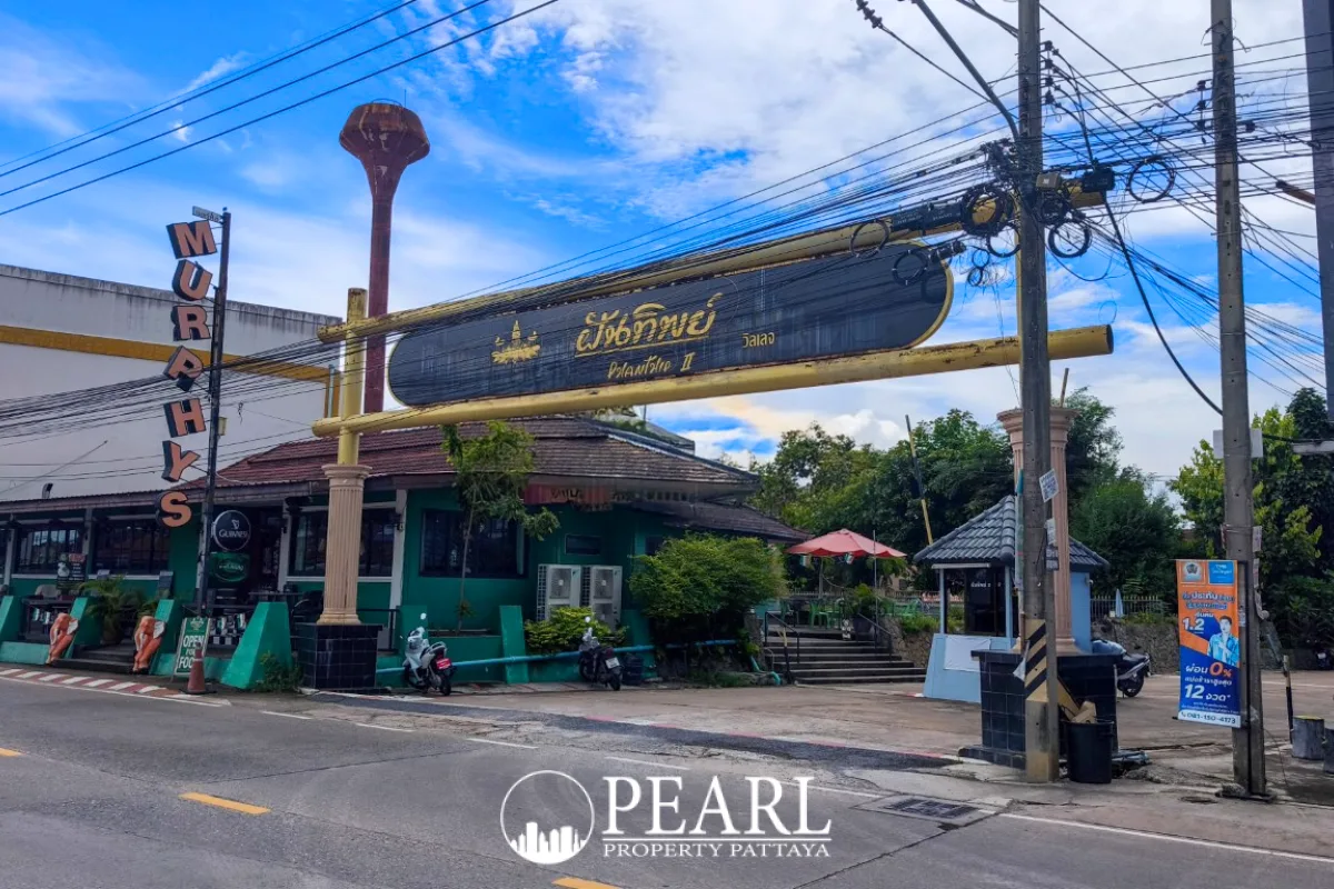 Phanthip Village 2 entrance sign in Thai and English, with a green restaurant building and a water tower in the background.