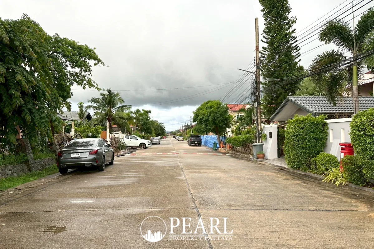 Phanthip Village 2 house exterior with a grey facade, black gate, concrete fence, and green hedges under a cloudy sky.