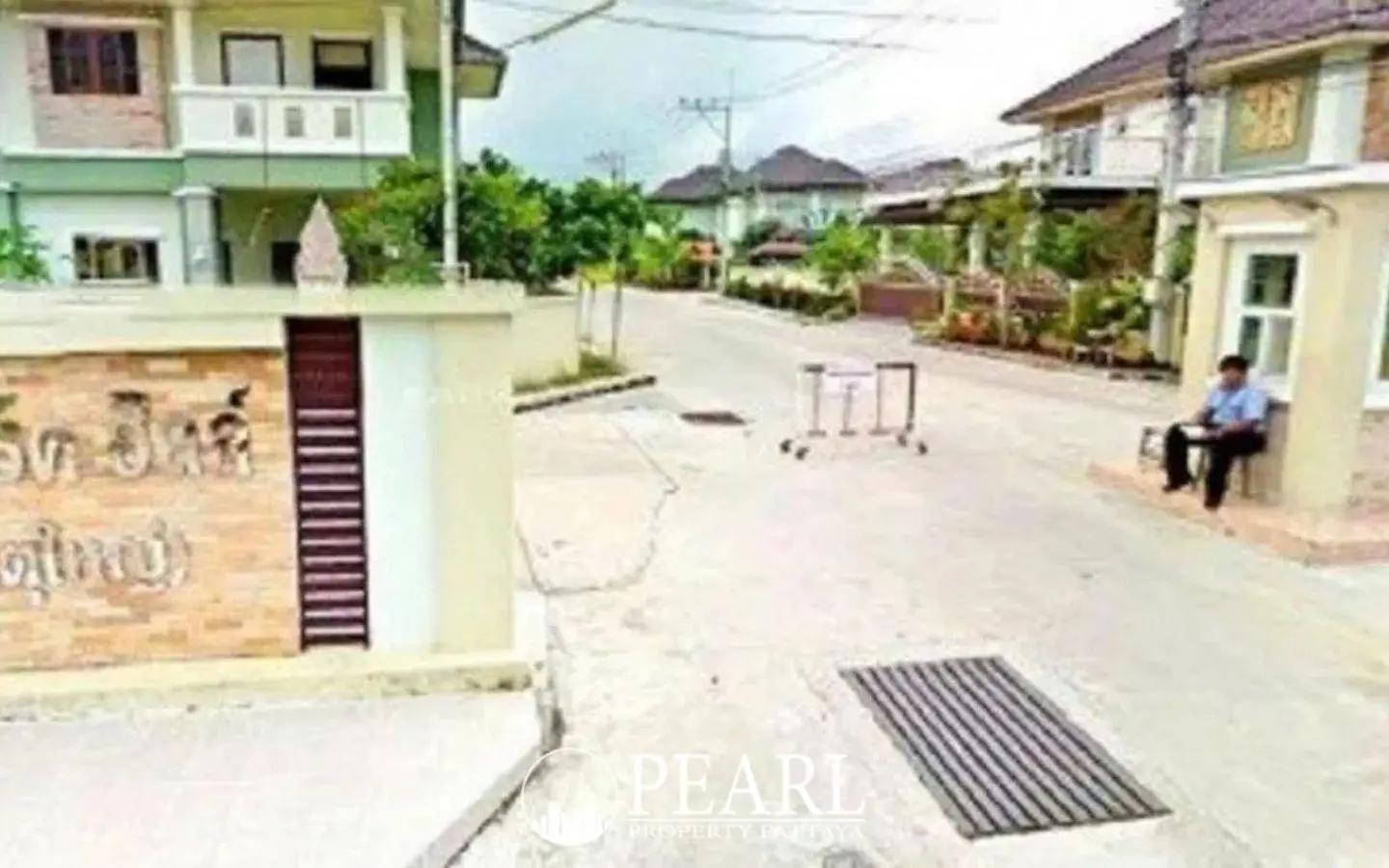 Park Hill Village entrance with a security guard sitting, a sign with Thai text, and houses in the background.