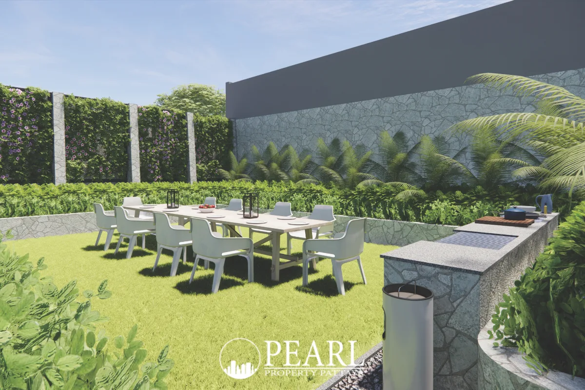 Siam Royal View Lakeside lush green garden with an outdoor dining table, chairs, and built-in barbecue area.