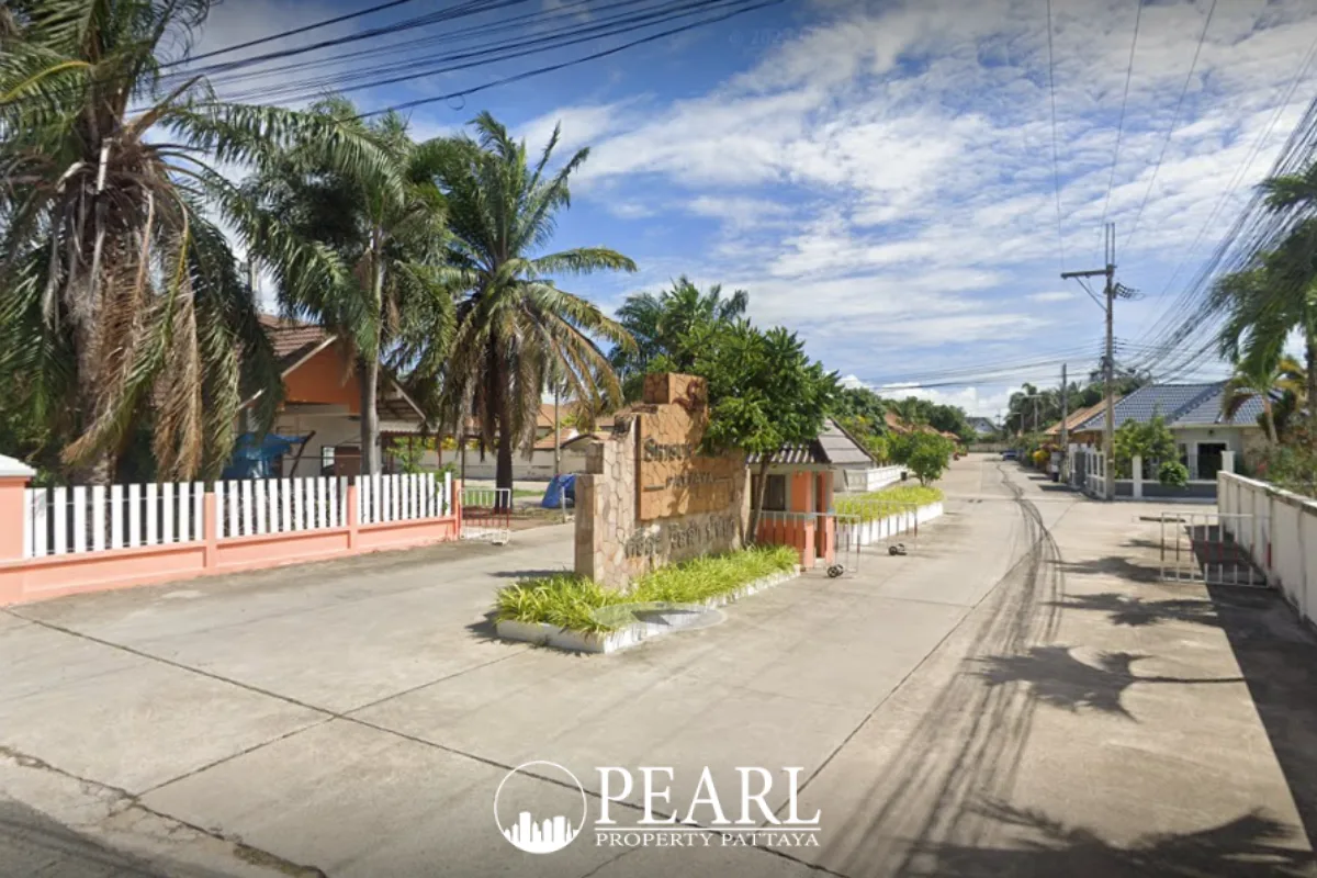 Srisuk Villa entrance gate with stone sign, palm trees, and residential road under a blue sky in Pattaya, Thailand.