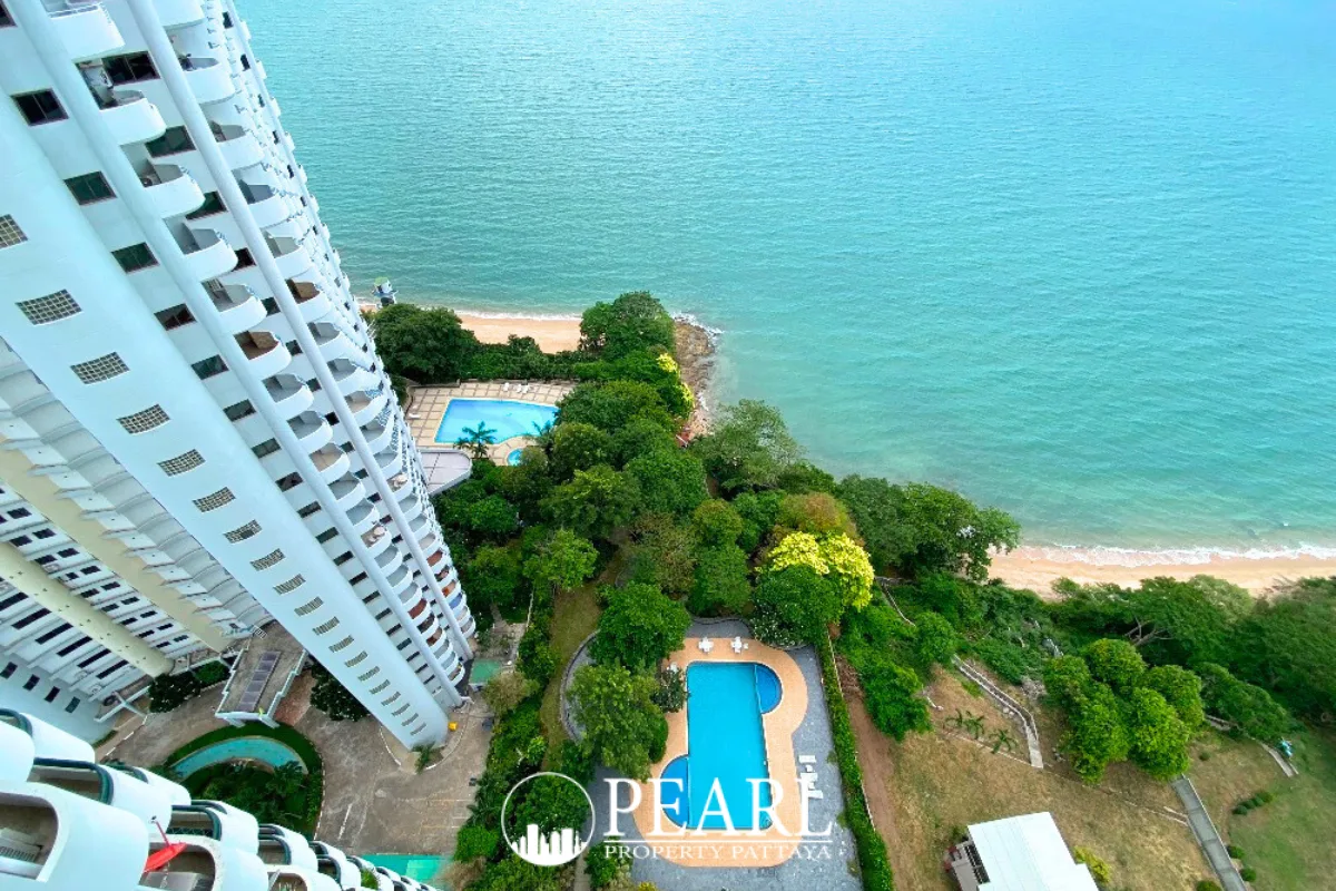 Sunset Heights Condominium: High-angle view of the building, two outdoor pools, green trees, and the blue ocean with a beach.