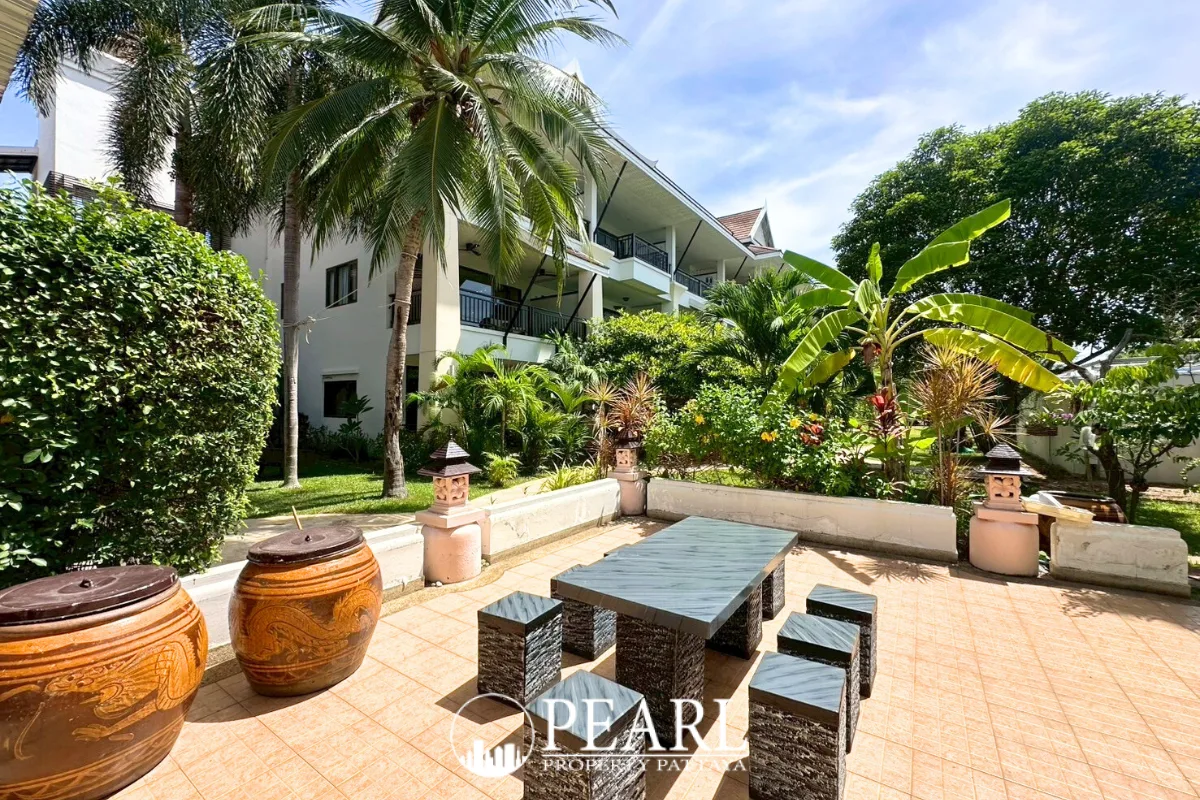 Sunrise Beach Residence outdoor patio with a dark grey table and stools, surrounded by tropical plants and palm trees.
