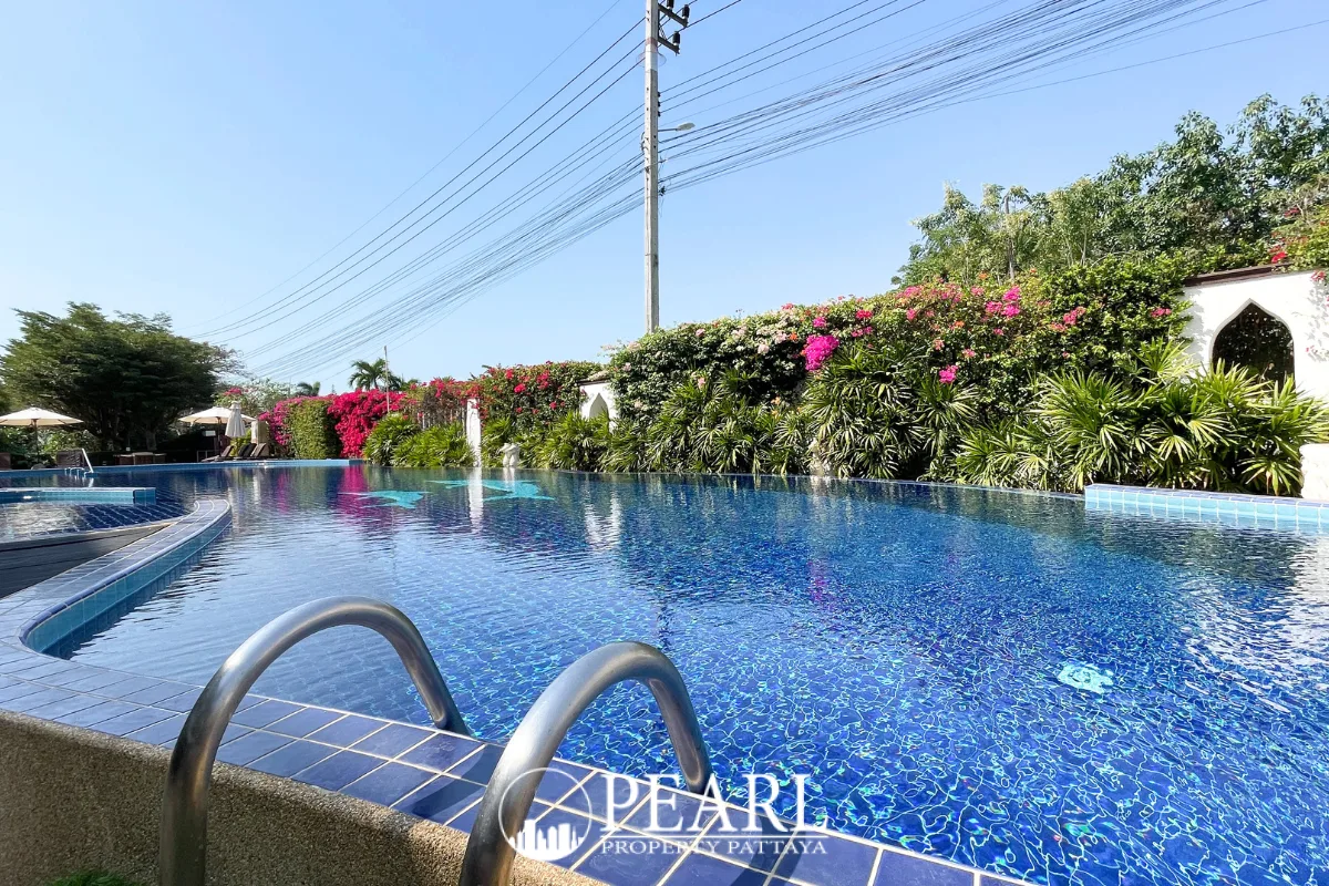 Sunrise Beach Residence large outdoor swimming pool with blue mosaic tiles, surrounded by lush greenery and flowering bushes.