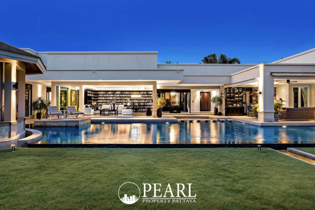 The Vineyard luxurious house exterior at dusk with a large swimming pool, illuminated living areas, and green lawn.