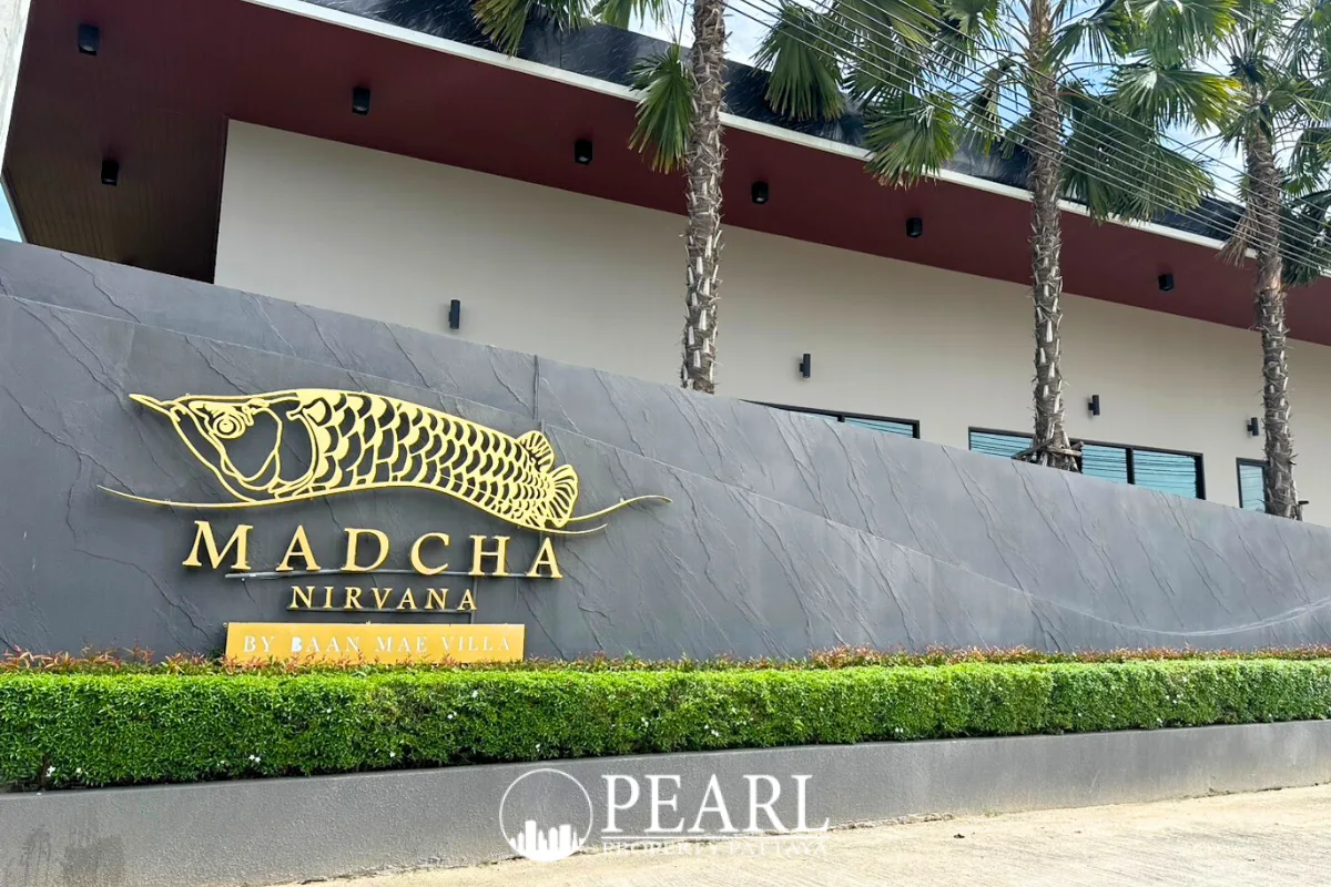 Madcha Nirvana property entrance sign with a golden fish logo, green hedge, and palm trees.
