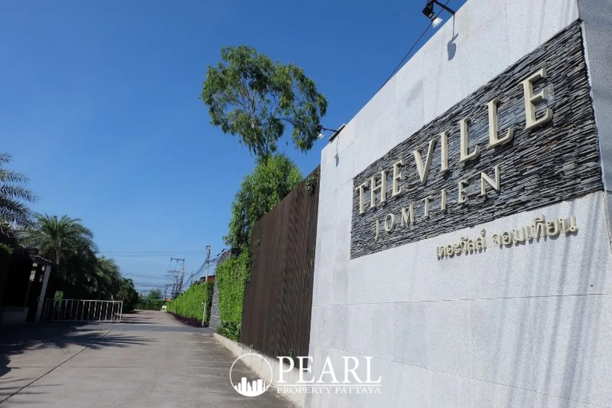 The Ville Jomtien main entrance gate with large stone sign under a clear blue sky.