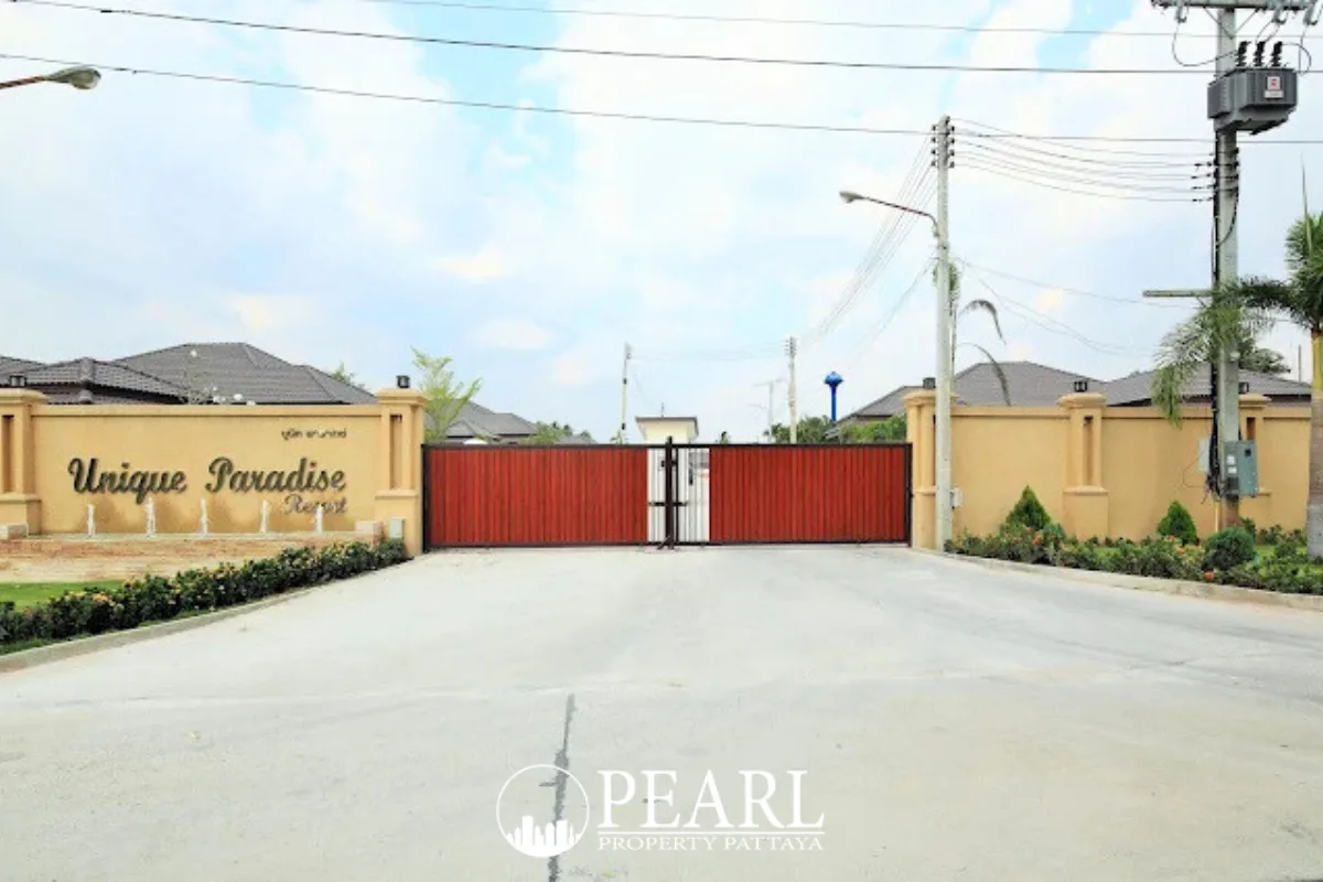 Unique Paradise Resort main entrance gate with resort name sign and surrounding houses under a cloudy sky.