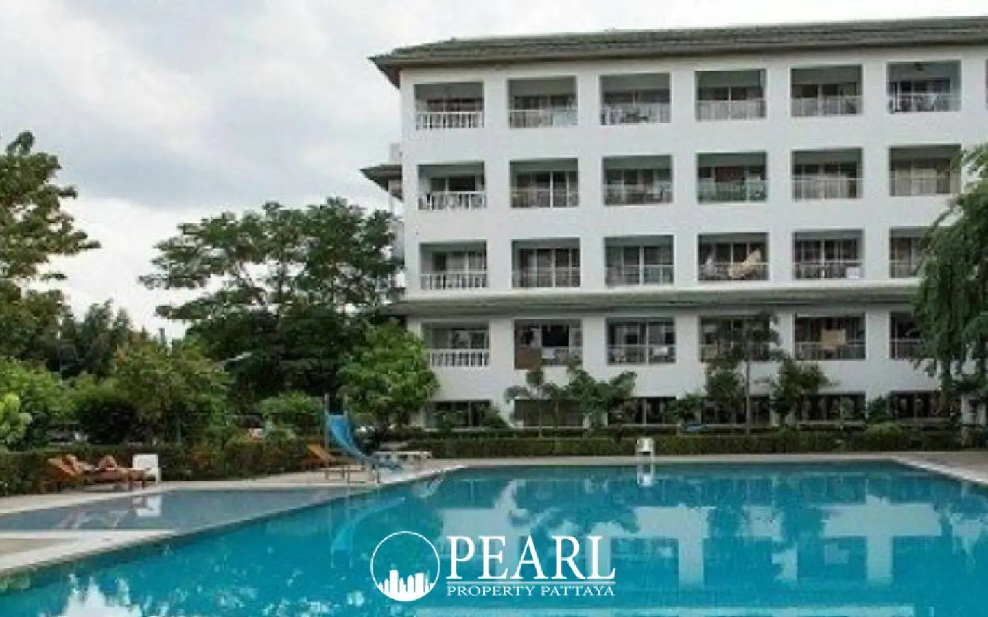 Baan Suan Lalana outdoor swimming pool with a slide and a white condo building surrounded by lush trees.