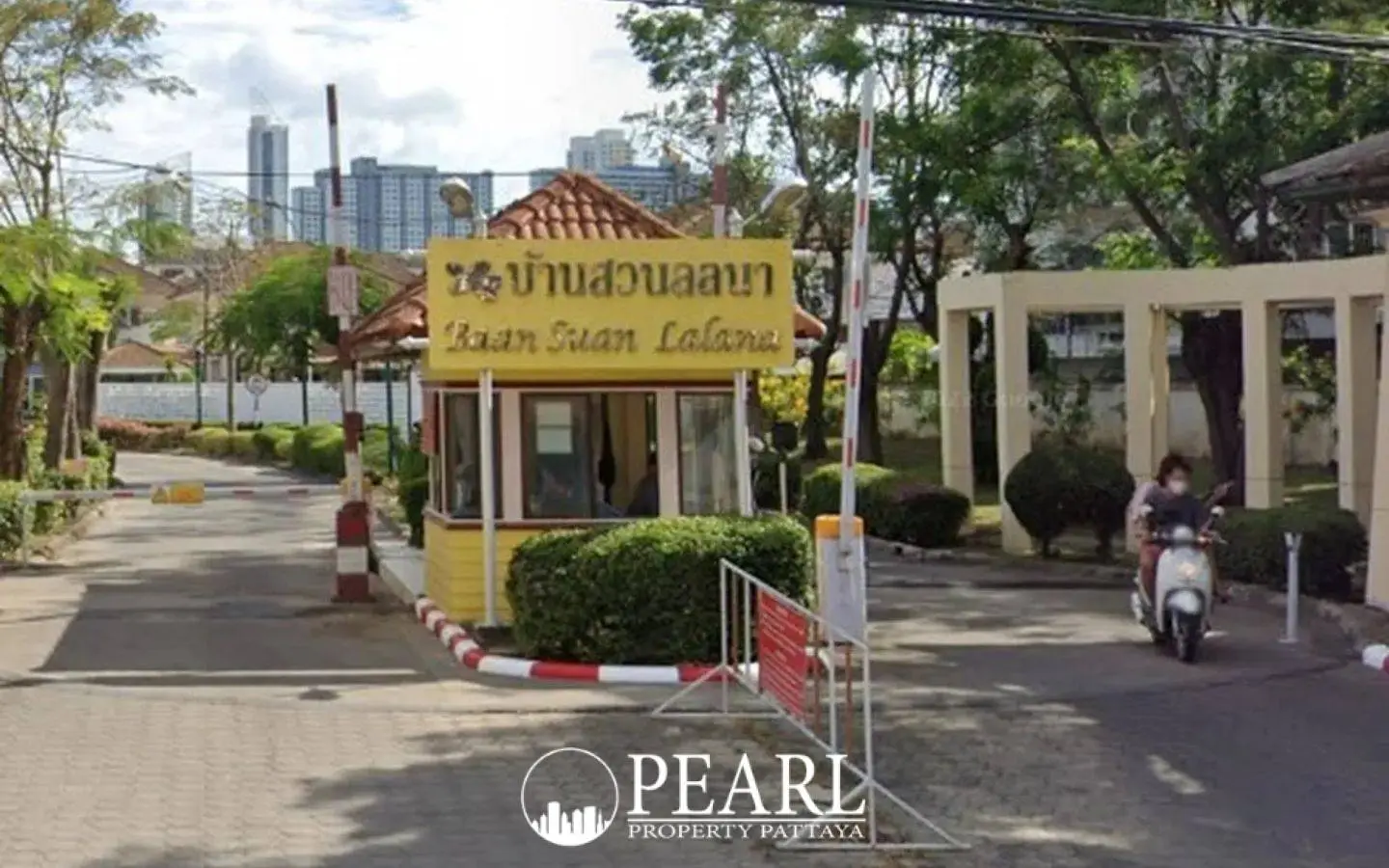 Baan Suan Lalana entrance gate with security booth, signage, and a person on a scooter.