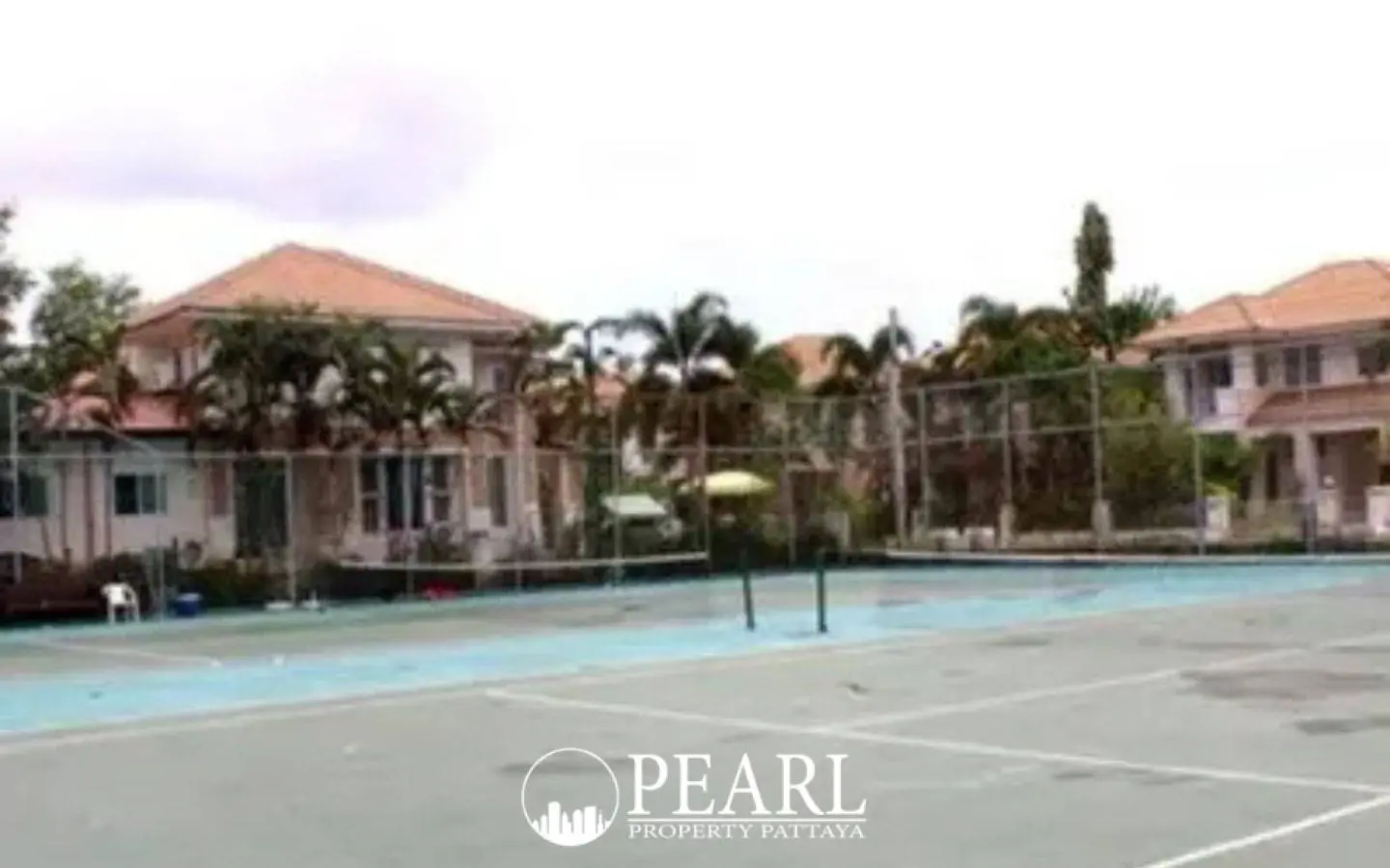 Baan Suan Lalana outdoor tennis court with residential buildings and palm trees in the background.