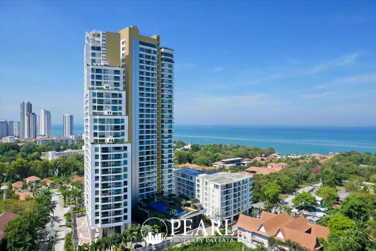The Peak Towers high-rise condominium building with multiple balconies, surrounded by green trees, overlooking the ocean.