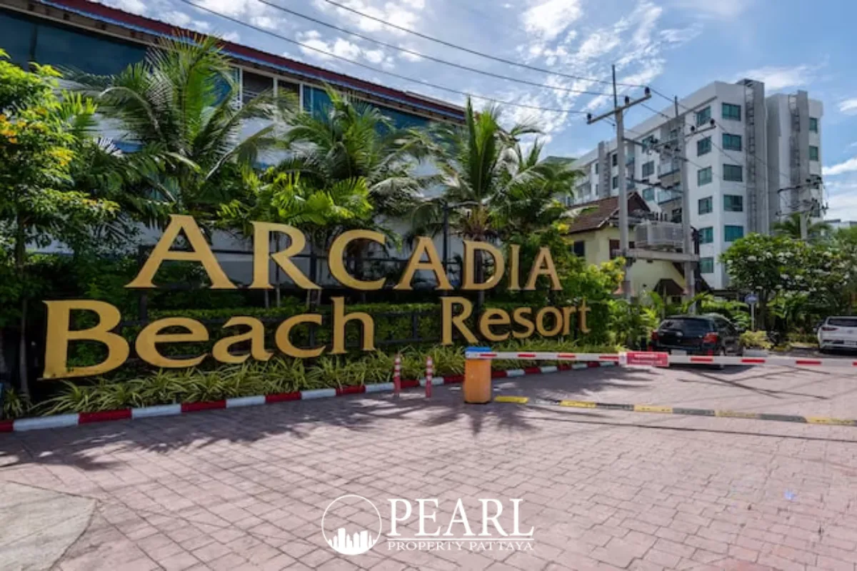 Arcadia Beach Resort entrance sign with golden letters, surrounded by tropical plants and resort buildings.