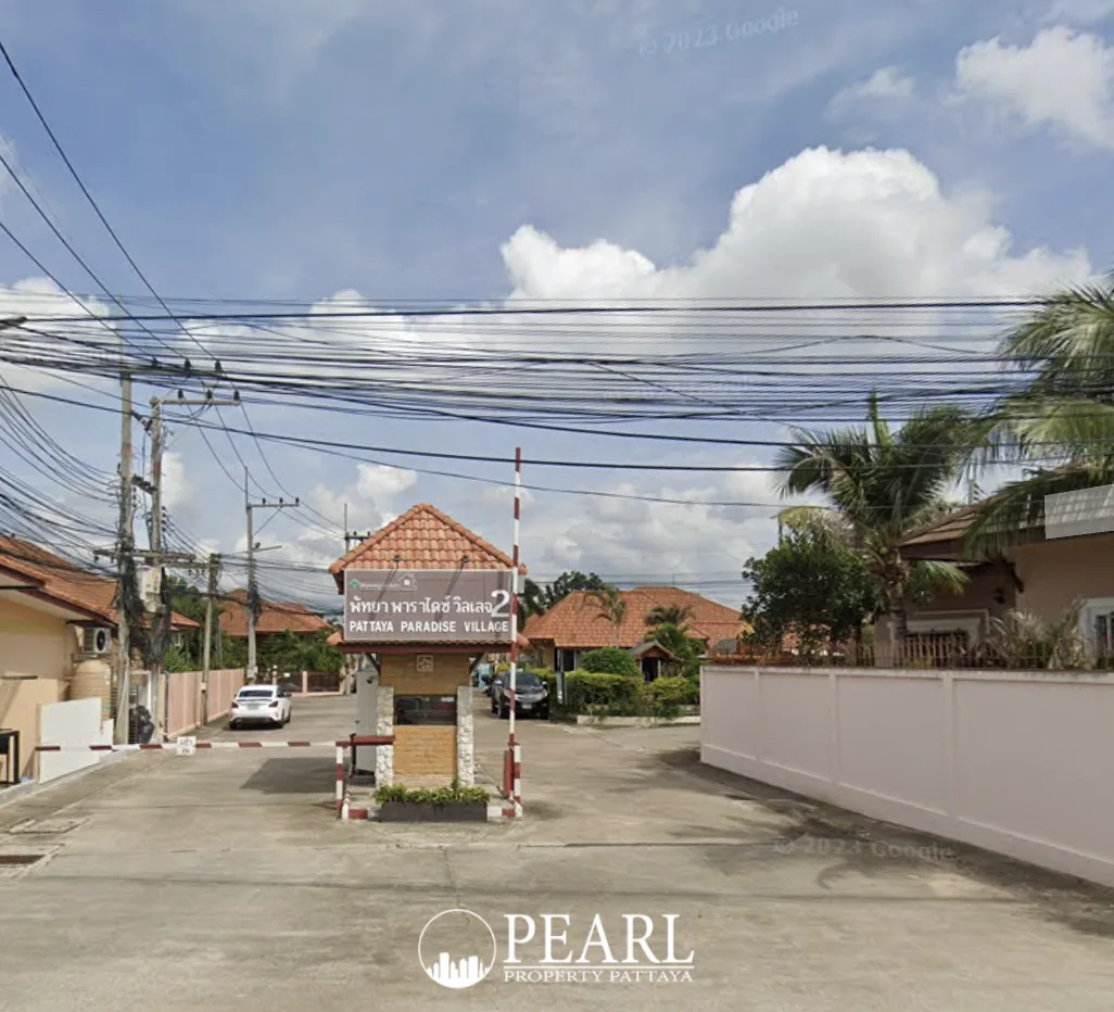 Pattaya Paradise Village 2 entrance gate with guard booth, barrier, and village sign under a cloudy sky.