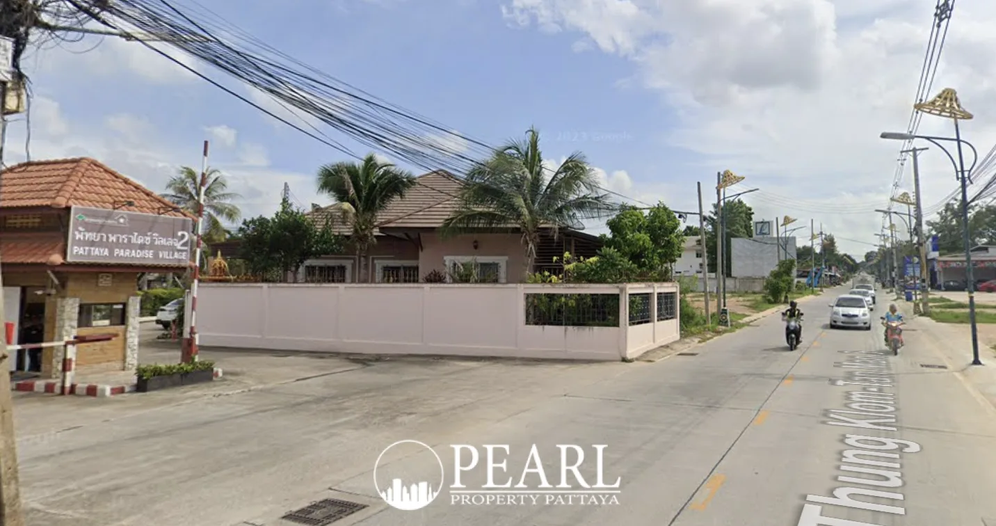 Pattaya Paradise Village 2 entrance gate from a wider street view with traffic and palm trees.