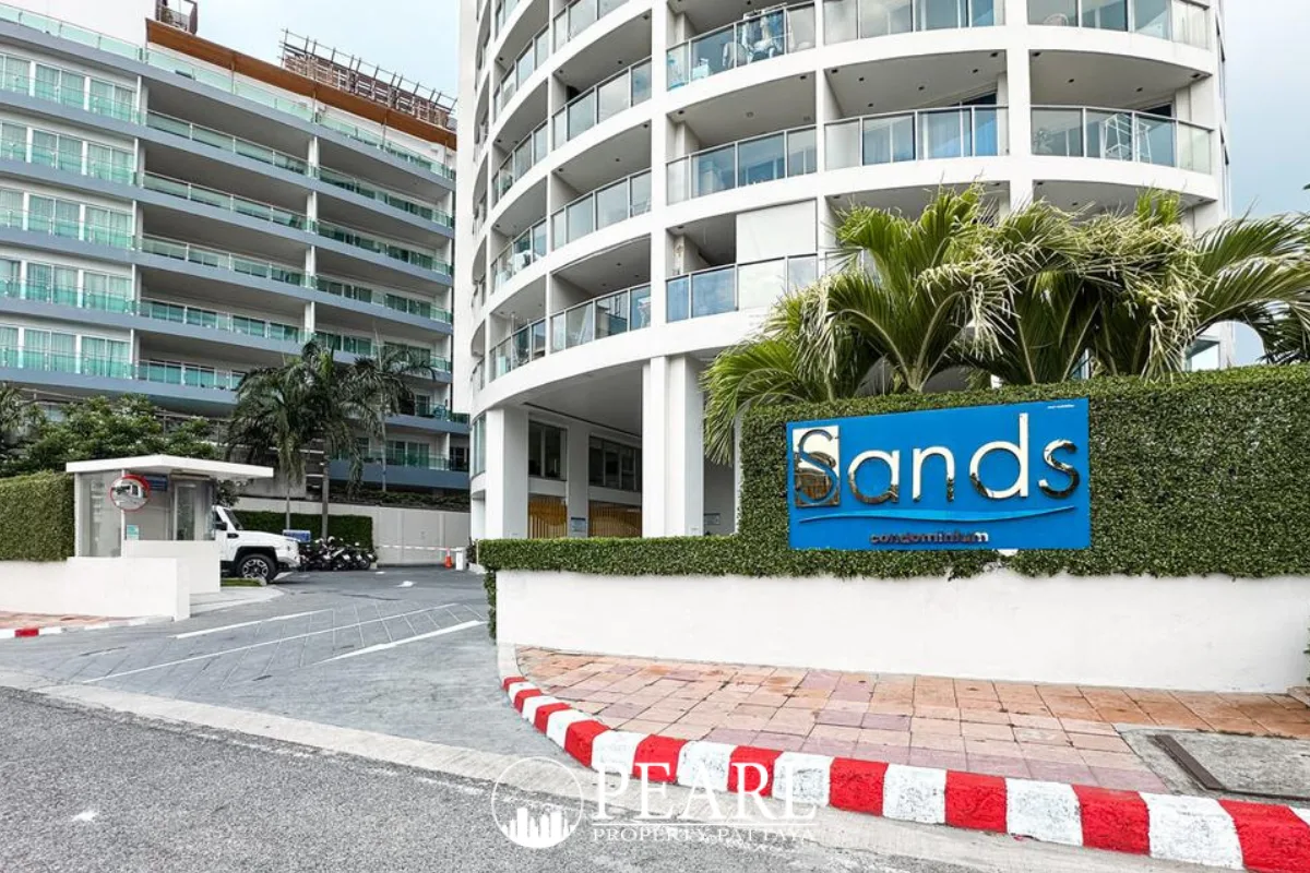 Sands Condominium main entrance with a blue sign featuring the property name, surrounded by green hedges.
