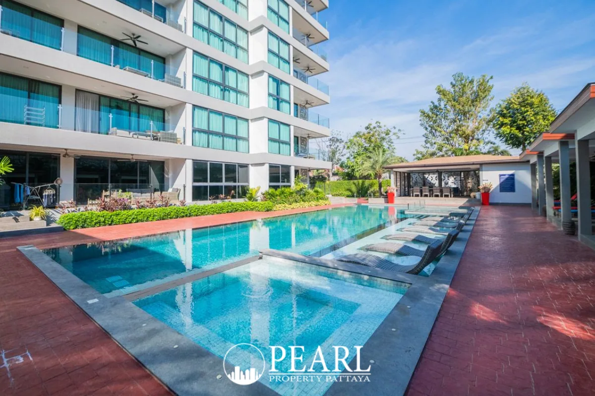 Serenity Residence Jomtien outdoor swimming pool area with lounge chairs and the apartment building in the background.